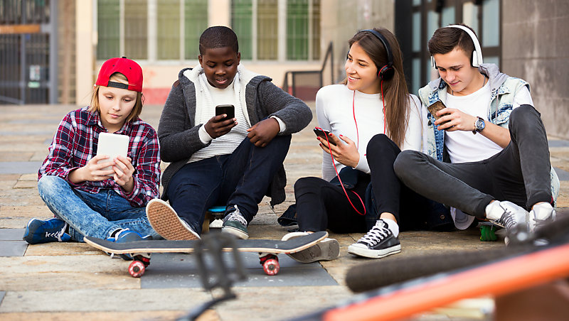 Teenagers, outdoors, checking their mobile phones.