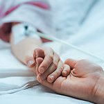 Recovering Little Child Lying in the Hospital Bed Sleeping, Mother Holds Her Hand Comforting. Focus on the Hands. Emotional Family Moment.