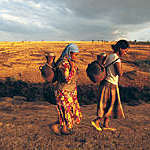Two African women carrying terracotta water pots on their backs.