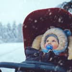 Baby boy in a stroller stares with bright blue eyes into a snowy winter landscape.